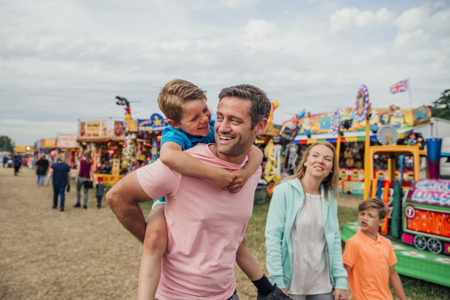 Family enjoying time at the fairground. Dad is carrying his son on his back